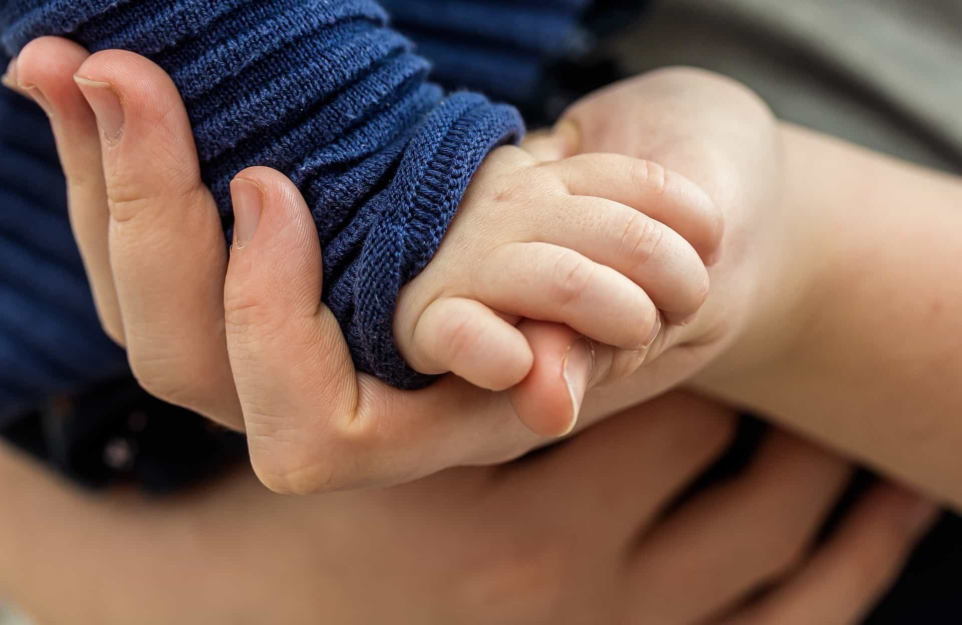 An adult hand holds a child's hand.
